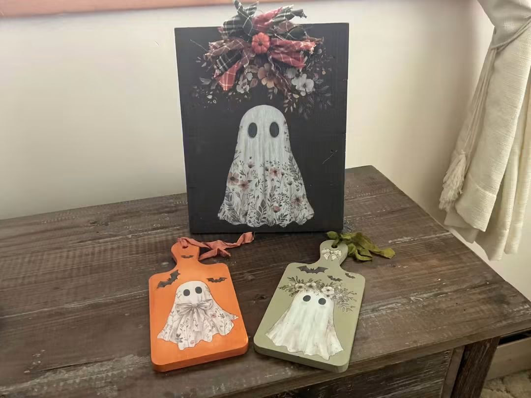 Tall ghost decoration with a bow beside orange and green ghost-themed tabletop pieces