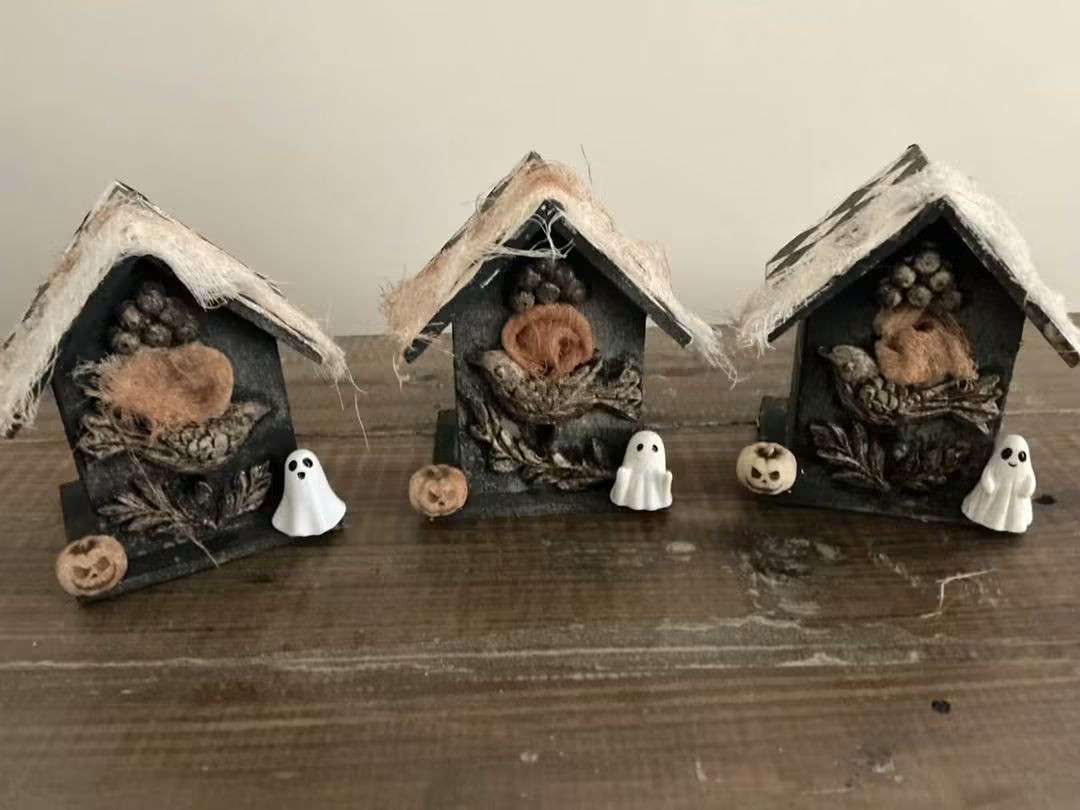 Three small house-shaped Halloween decorations with pumpkins and little white ghosts