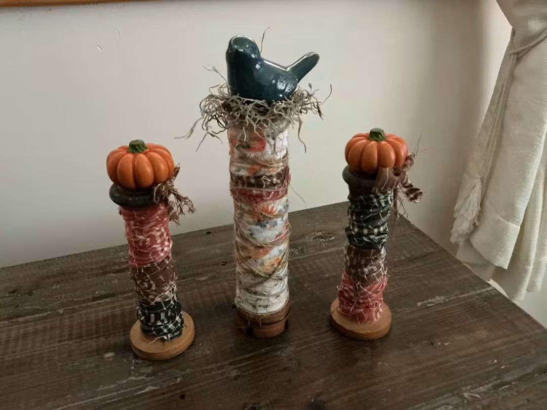 Three spool-shaped decorative accents topped with pumpkins and a blue bird